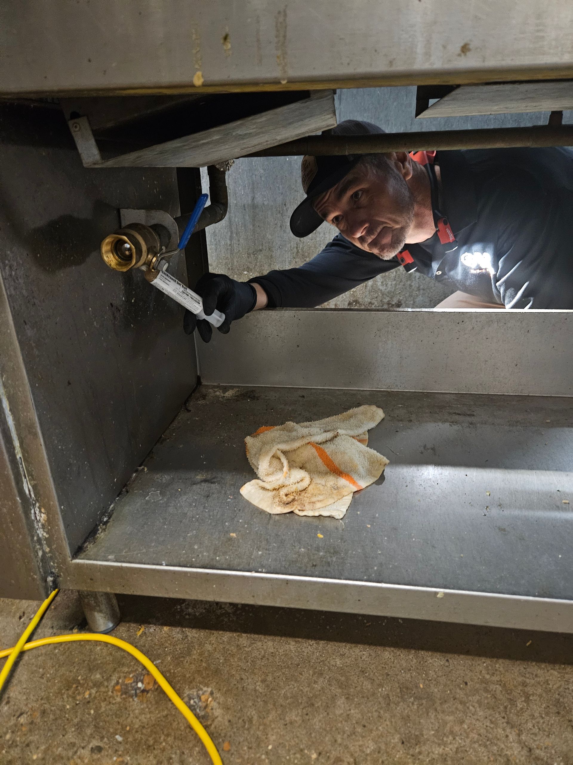 Person working under a metal structure with a wrench, near a cloth and yellow cable on the floor.