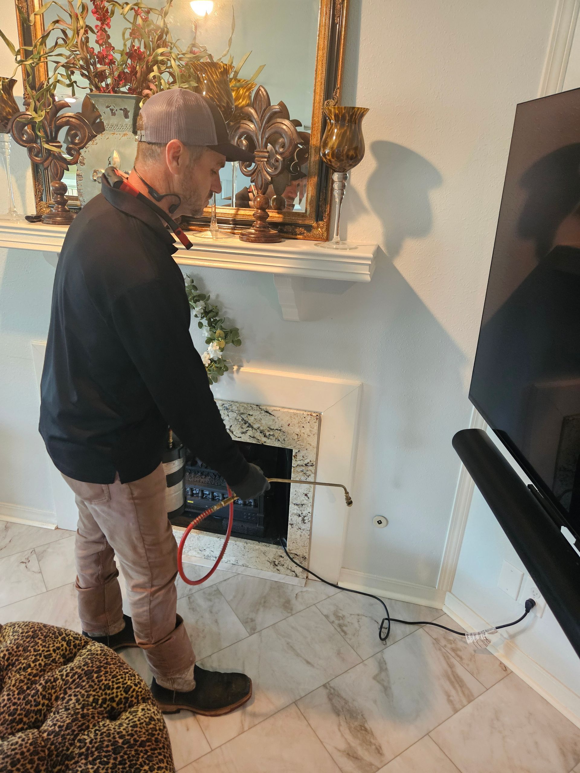 Man standing by a fireplace, using a red hose in a living room with decorative mantle items.
