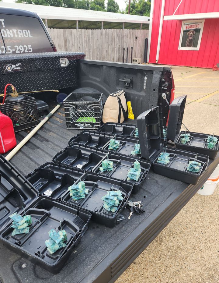 Open case of black electronic devices on a truck bed beside a red building