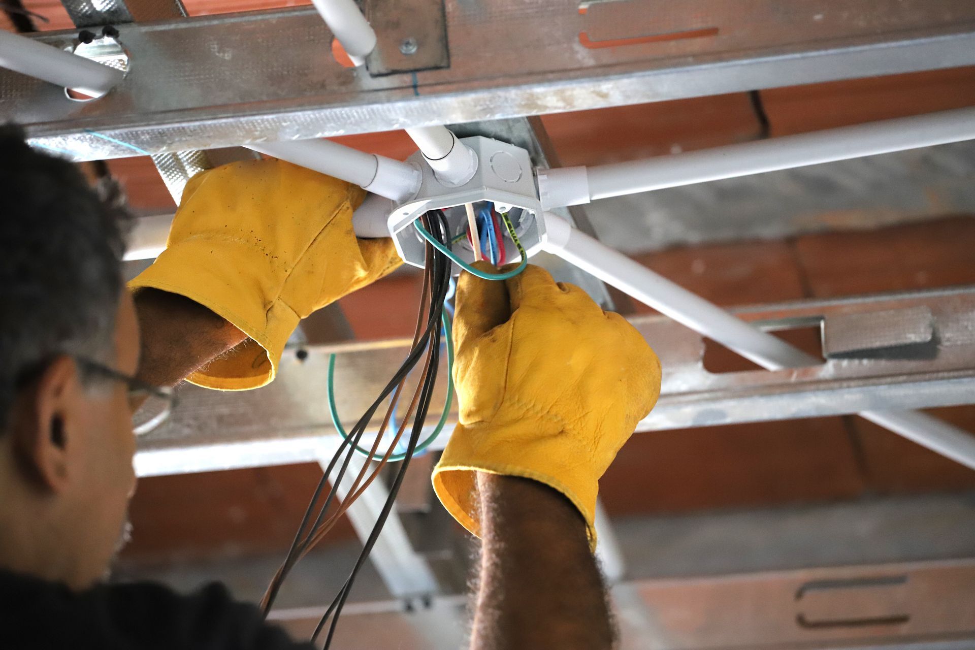 Person in yellow gloves wiring a ceiling light fixture amid exposed beams
