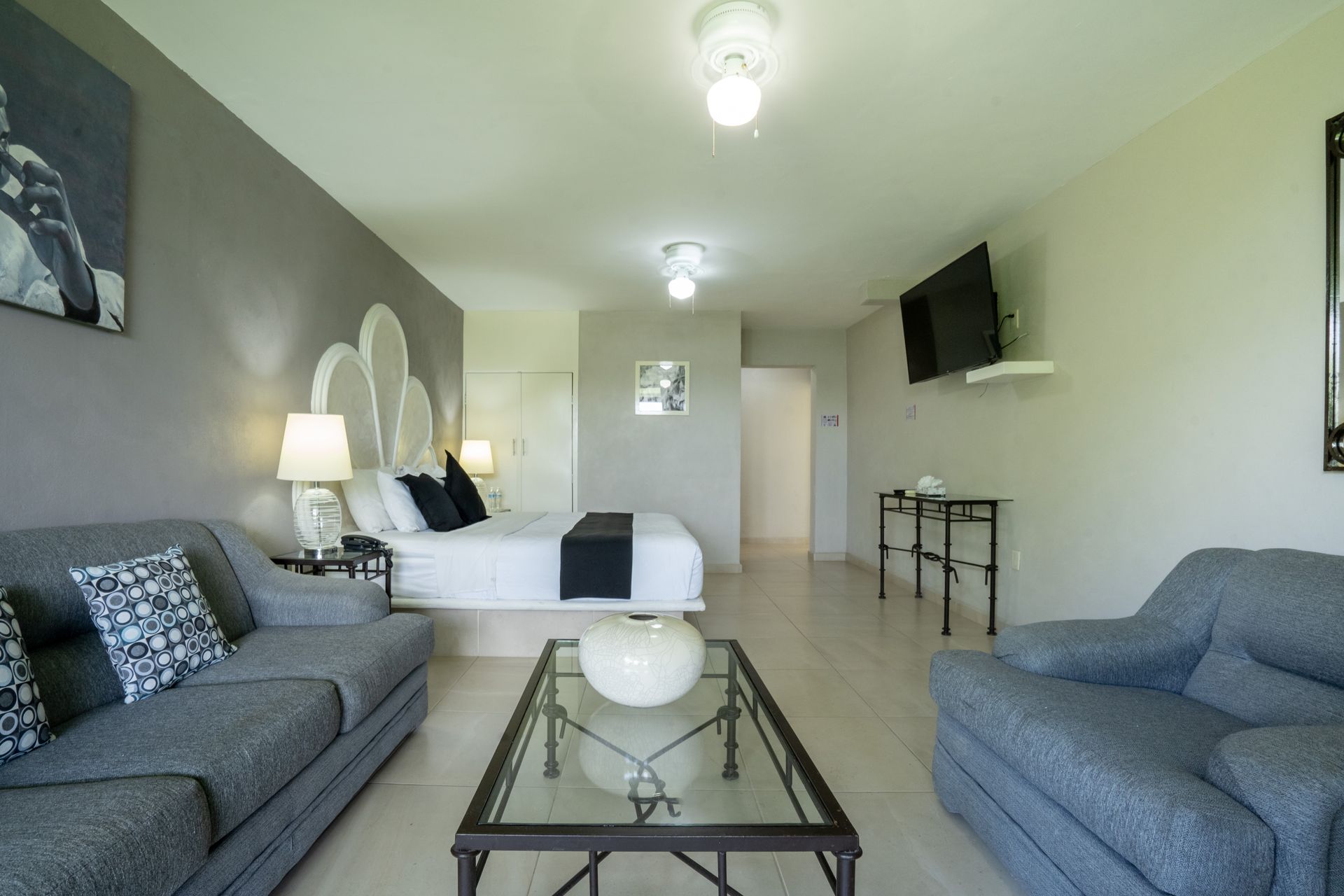 Apartamento tipo estudio gris y blanco con cama, sofá y TV.