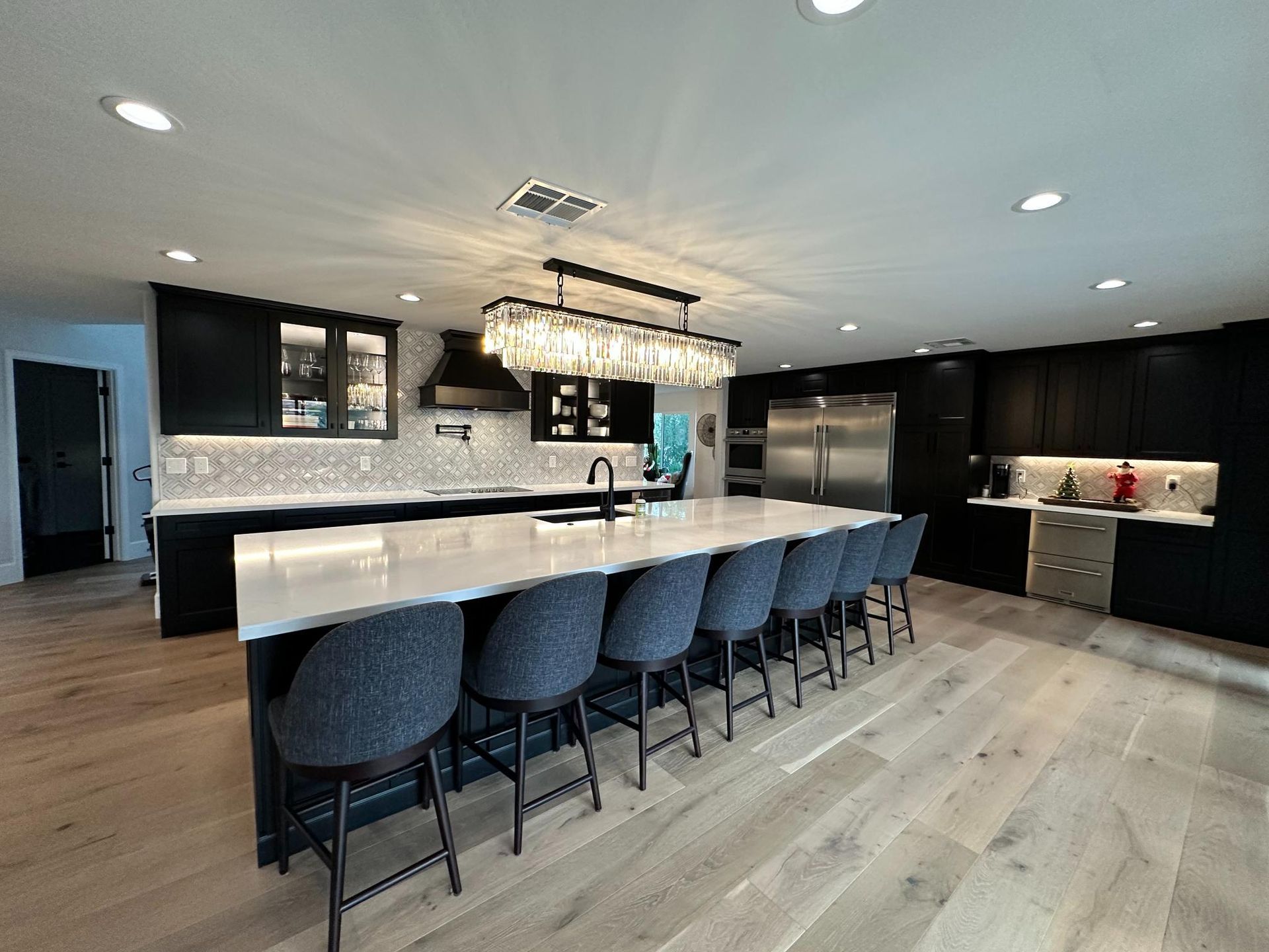 Modern kitchen with black cabinets, white countertops, large island with seating, and wood floors.