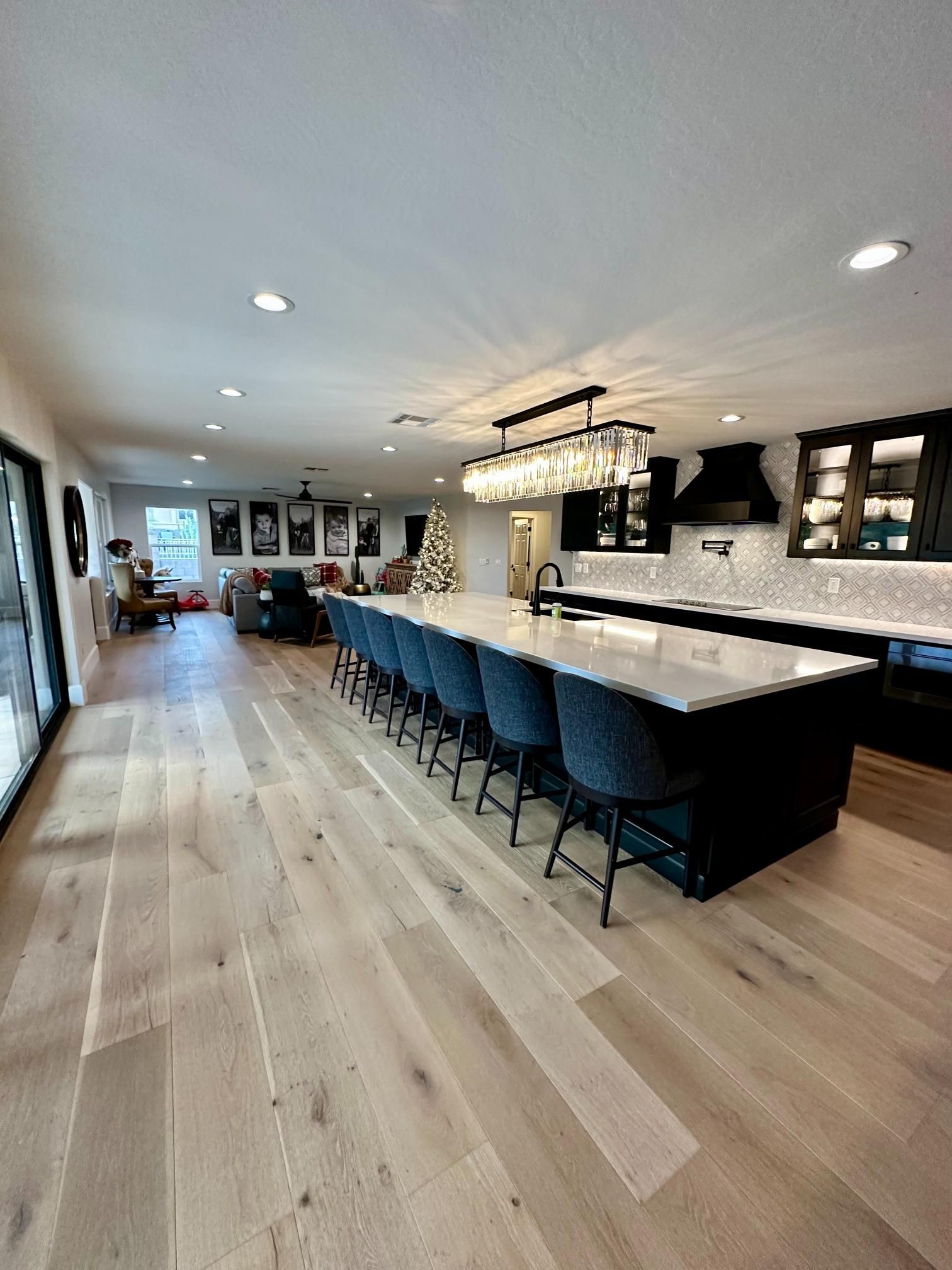 Spacious modern kitchen with long island, light wood floor, and blue bar stools. Open to living room.