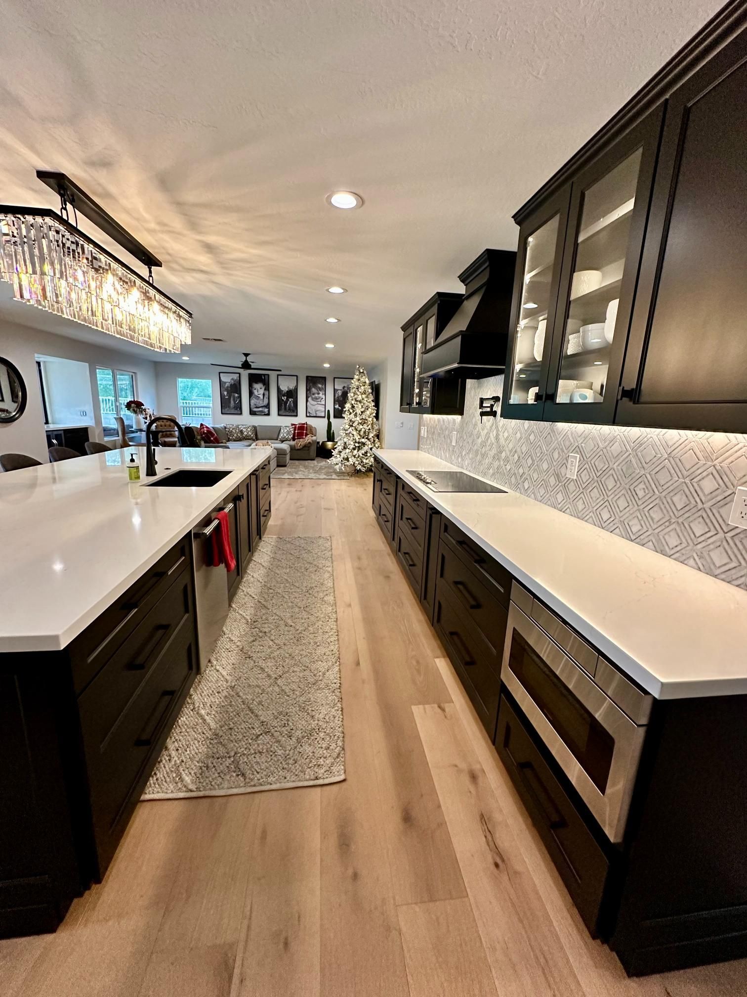 Modern kitchen with dark cabinets, white countertops, and light wood floors.