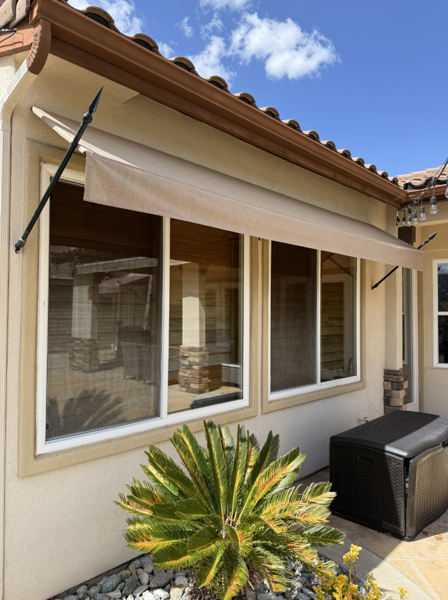 A house with a awning over the windows and a palm tree in front of it.