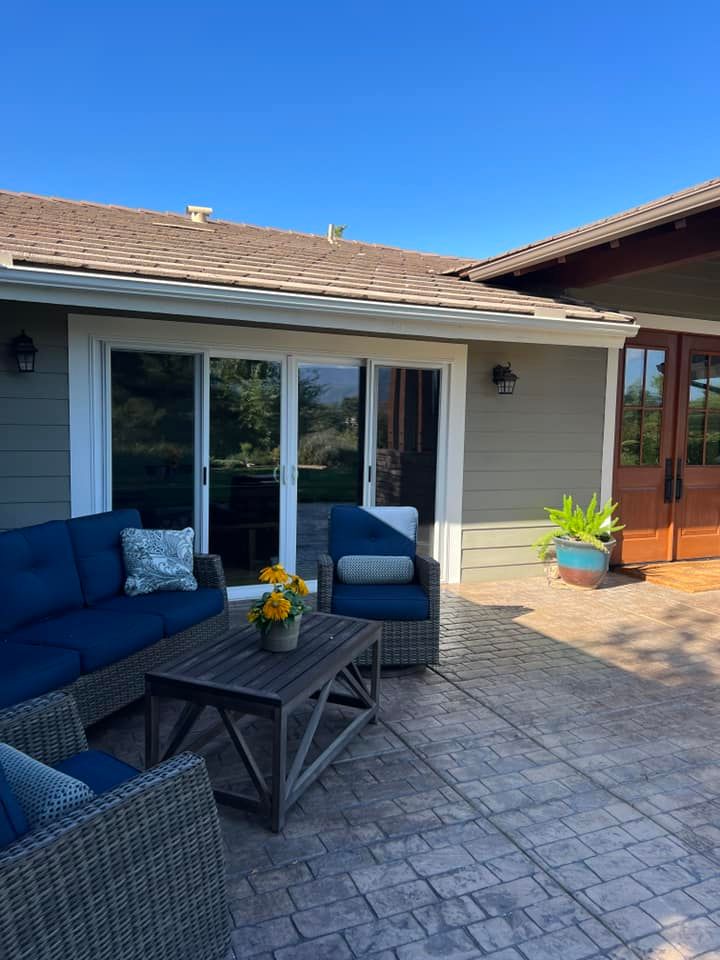 A patio with a couch , chairs and a table in front of a house.