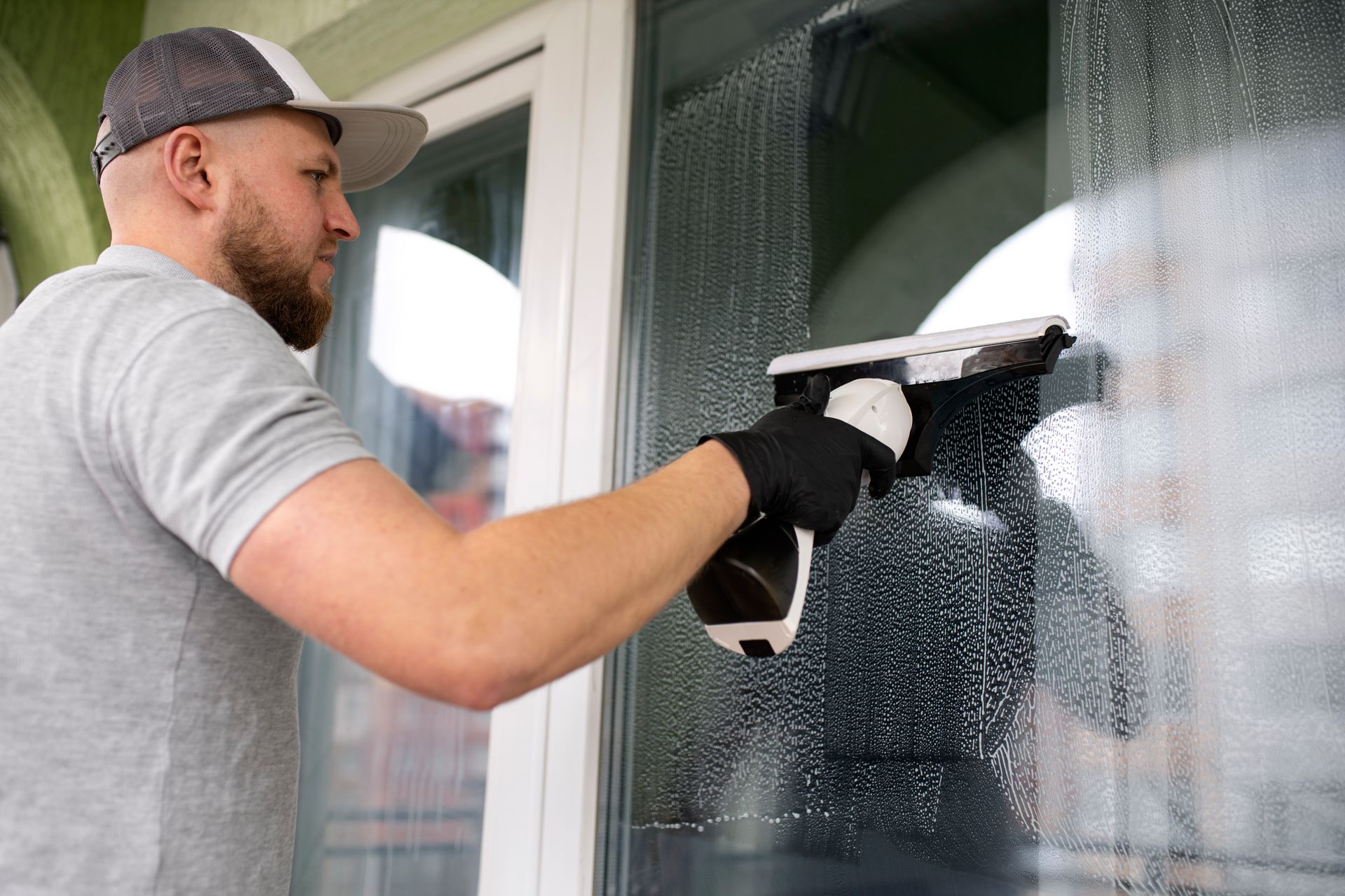 Man cleaning a window with a squeegee, washing suds from a glass door outdoors