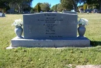 Gray granite cemetery headstone with vases on either side, standing in a grassy memorial area.