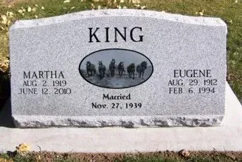 Gray gravestone engraved “KING” with names Martha and Eugene and a wedding scene oval.