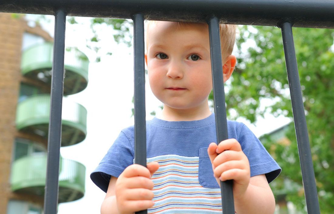 Child holding black bars outdoors, wearing a blue striped shirt with a neutral expression.