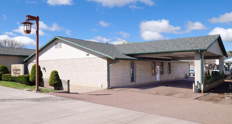 Single-story motel building with covered drive-up entrance and parking lot under a blue sky