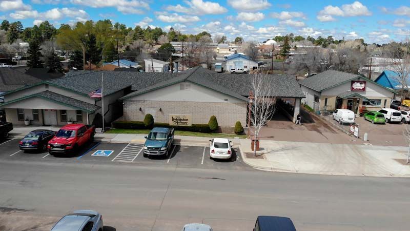 Aerial view of a single-story building with parked cars, accessible spaces, and trees under a partly cloudy sky