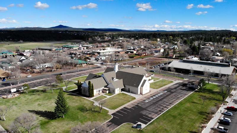 Aerial view of a small town with a church, parking lot, and surrounding buildings under a partly cloudy sky