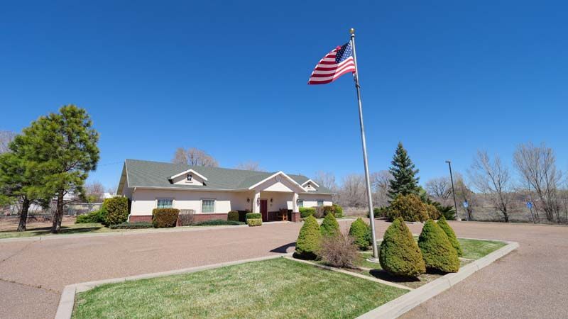 Single-story suburban house with an American flag, landscaped yard, and clear blue sky