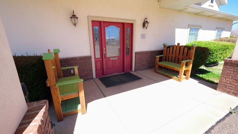 Front entrance with red double doors, benches, and potted plants on a sunlit patio