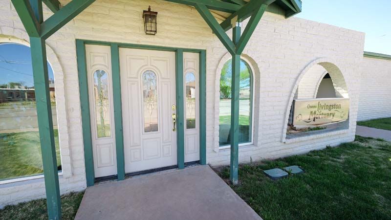 Small white chapel entrance with green trim, arched window, and a covered porch in a grassy setting
