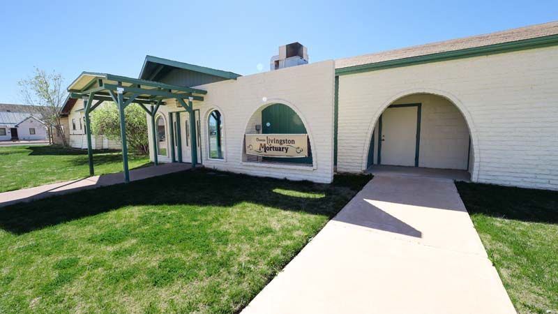 Single-story beige building with arched entryways and a sidewalk in front, on a sunny day