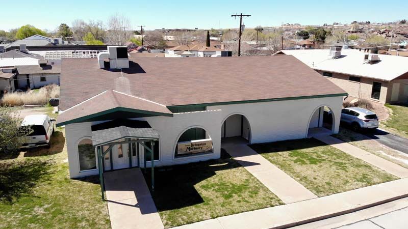 Aerial view of a beige single-story house with a brown roof, front arches, and a small lawn by the street