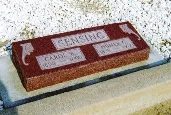 Carved red memorial marker on a stone base with “SENSING” and two name plaques.