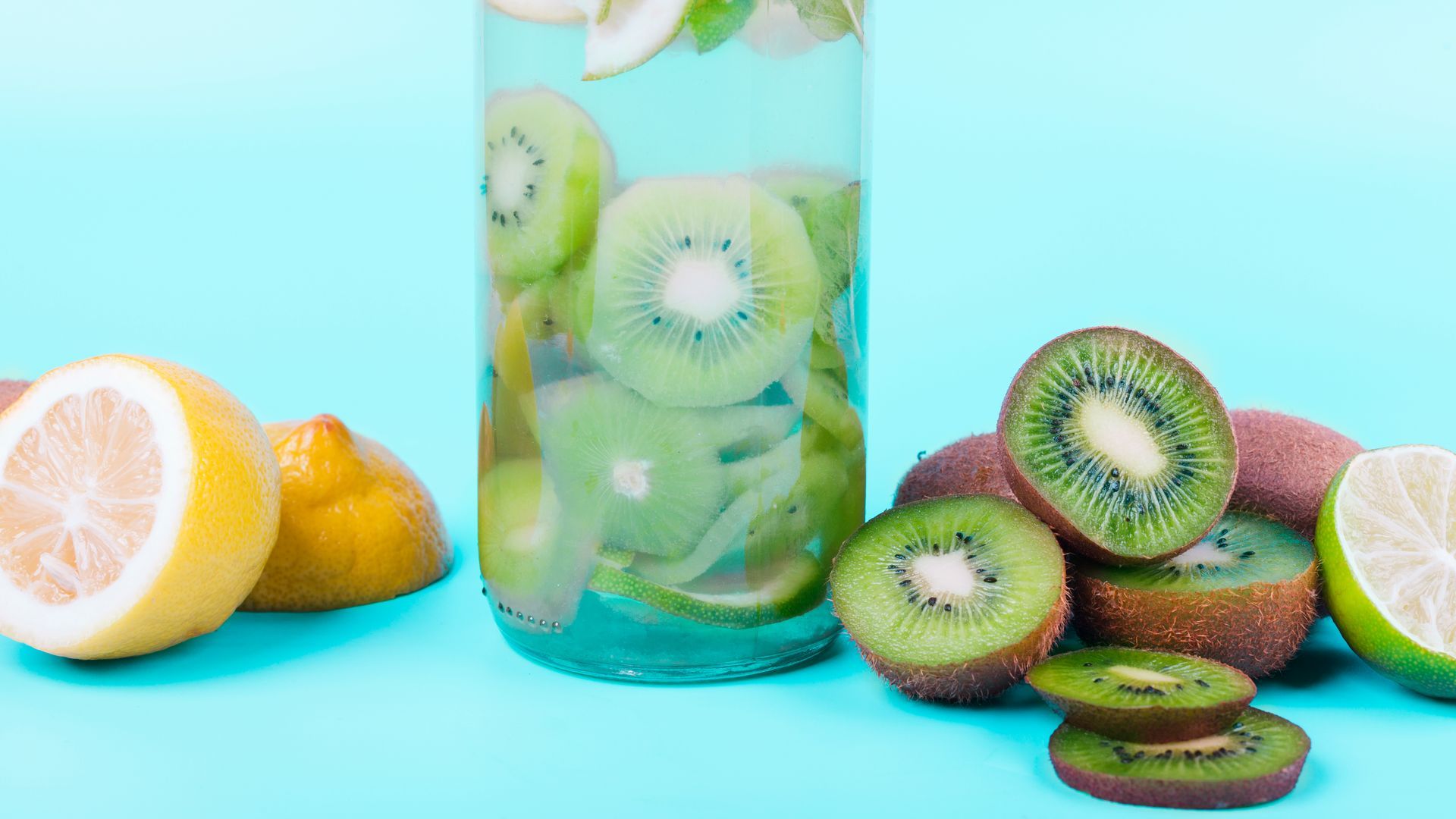 A glass of water with kiwi slices and lemon slices on a blue background.