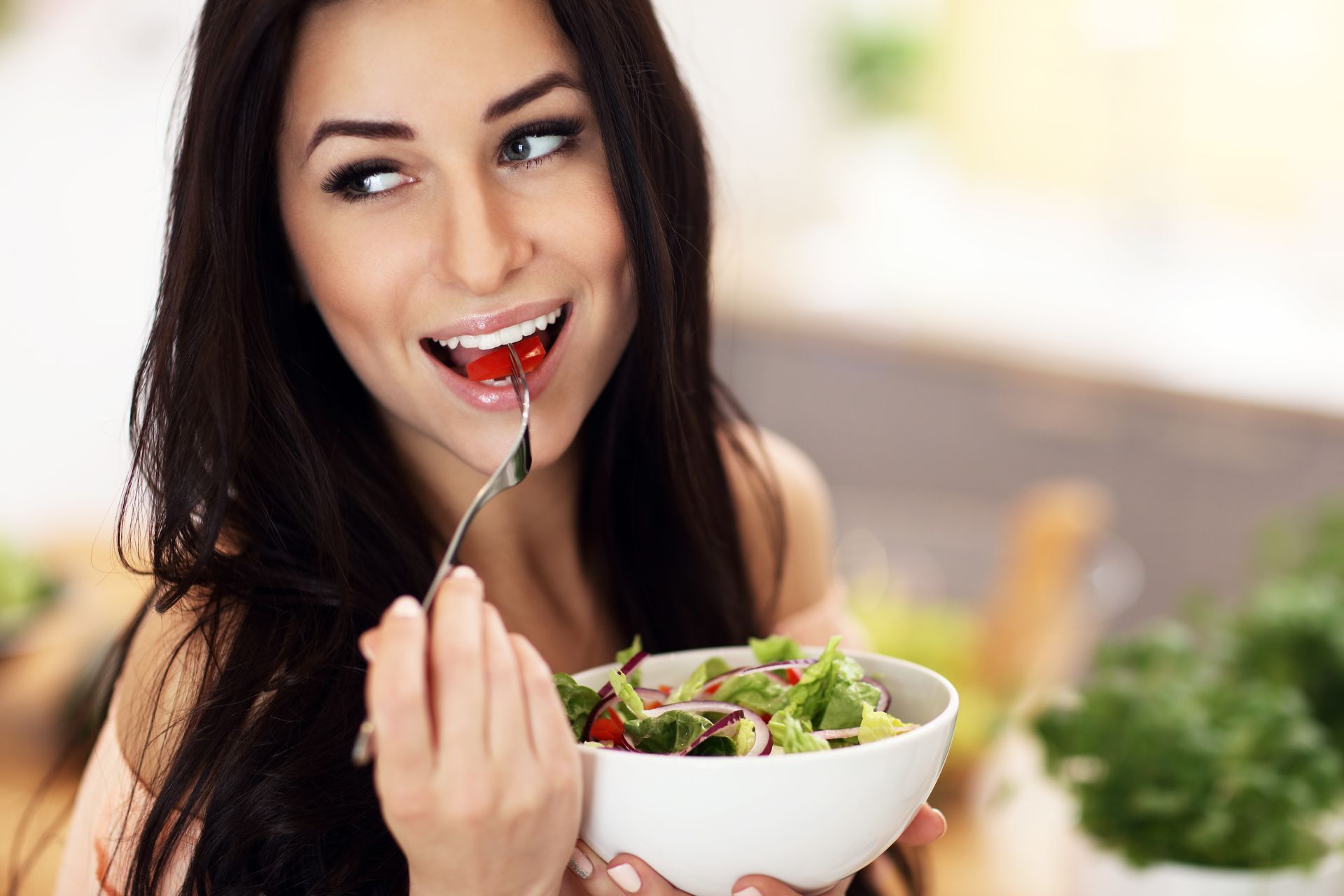 A woman is eating a salad from a bowl with a fork.