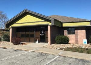 Exterior of a single-story brick building with a glass front door and accessible parking sign.