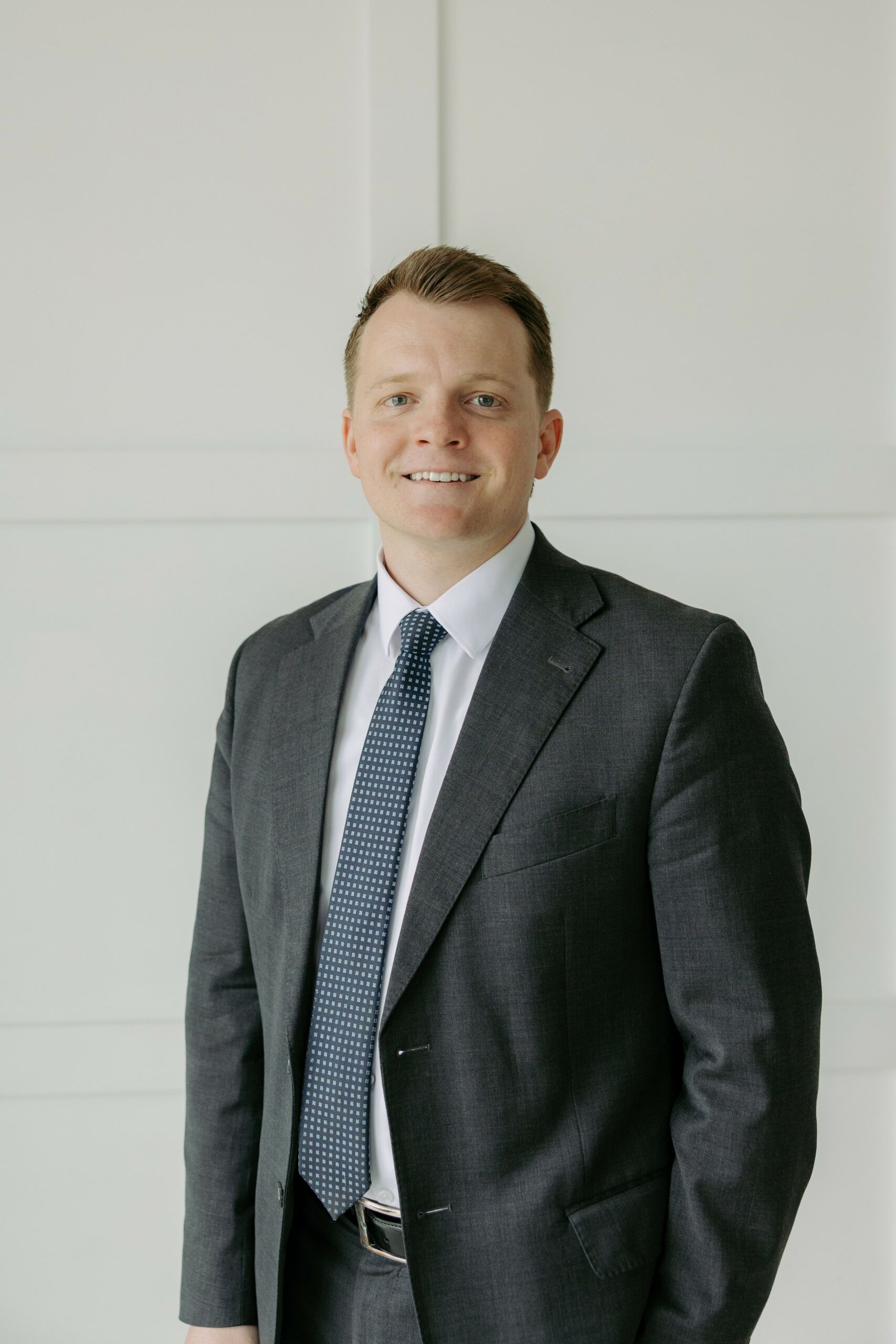 Man in a gray suit and blue tie smiling against a light wall
