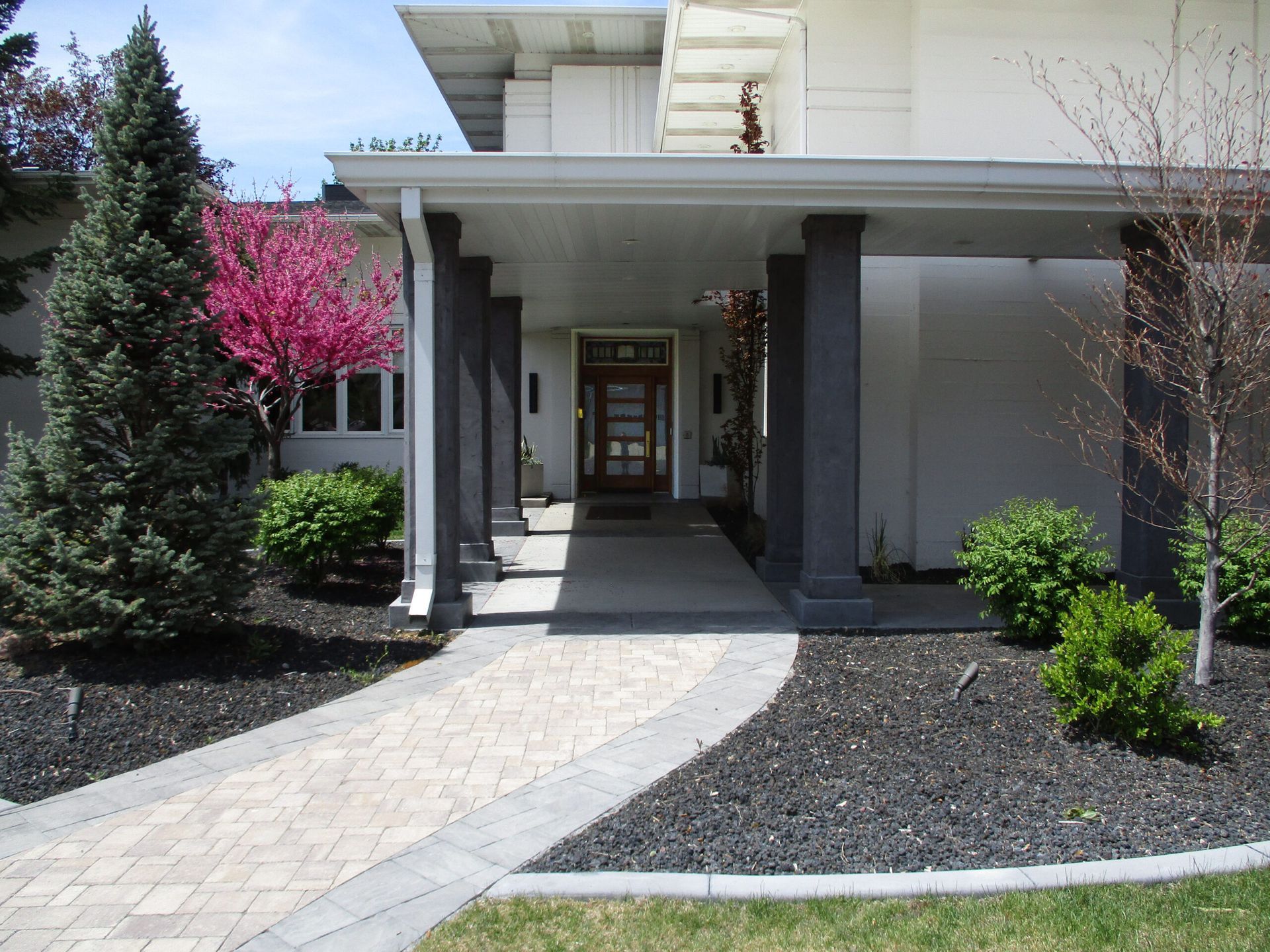 Modern house entrance with covered walkway, gray columns, and a curved stone path through landscaped front yard