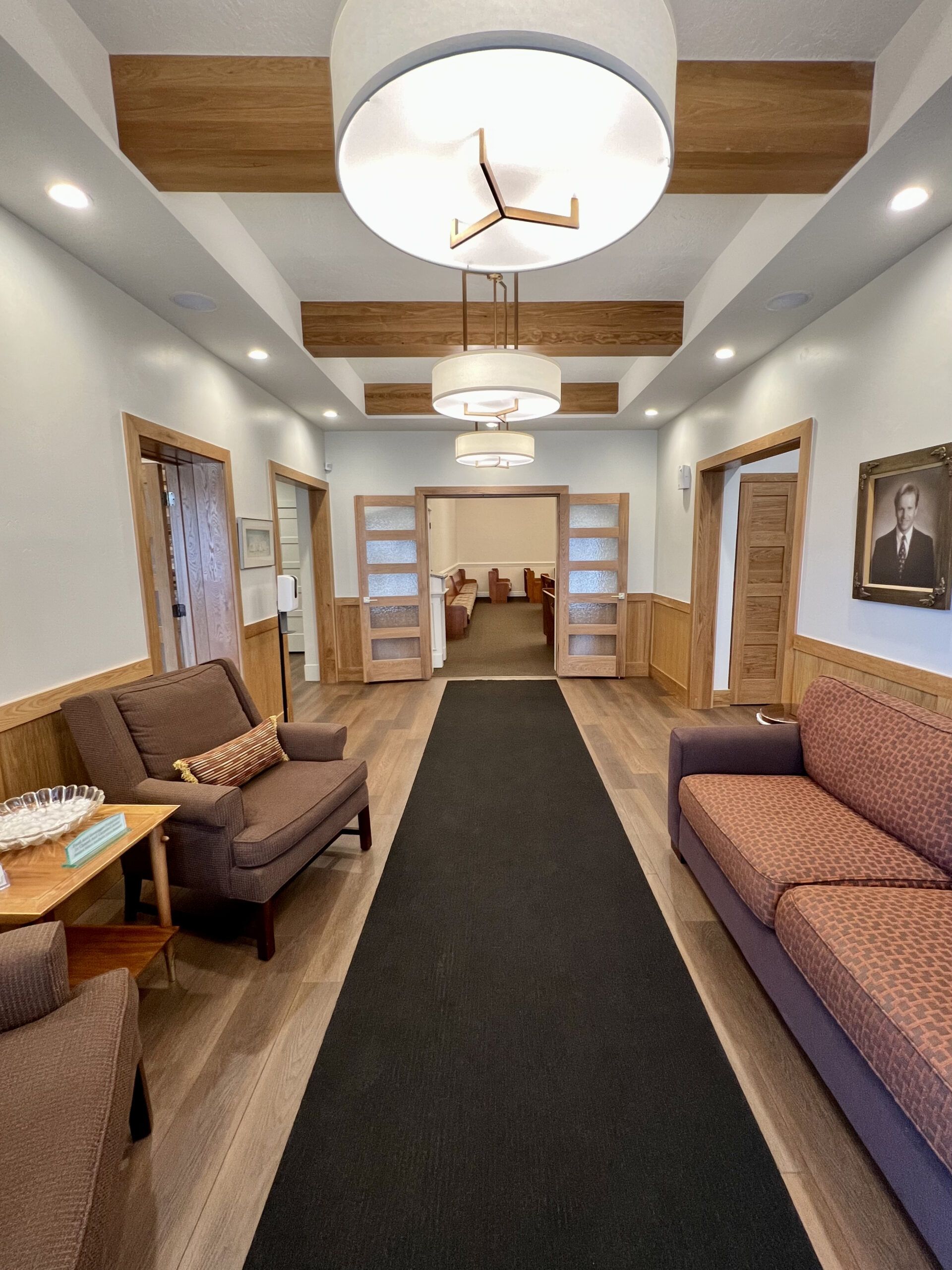 Bright waiting room with brown sofas, black runner, wood beams, and a small dining area in back
