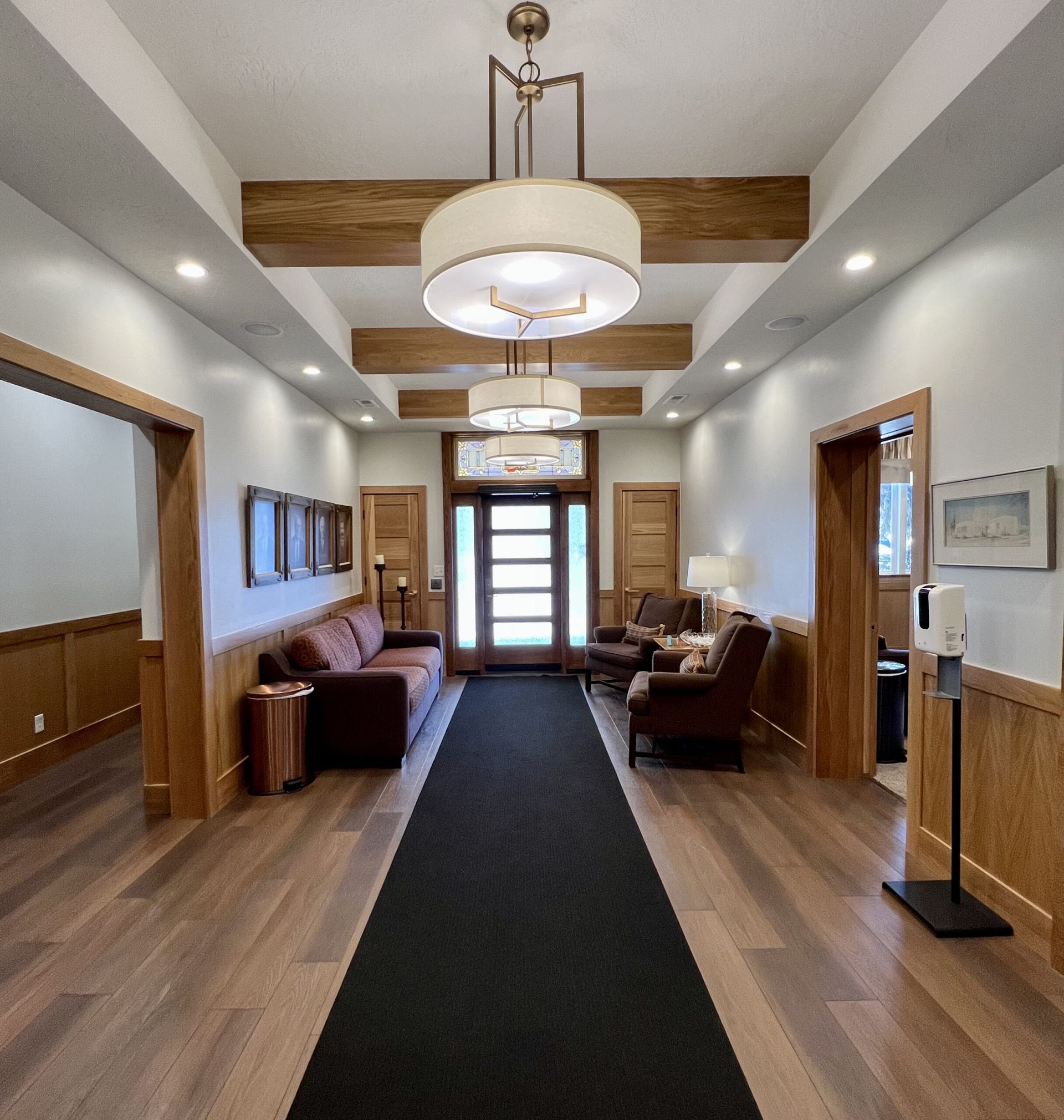 Long hallway with wood trim, brown chairs, black runner, and ceiling lights leading to double doors.