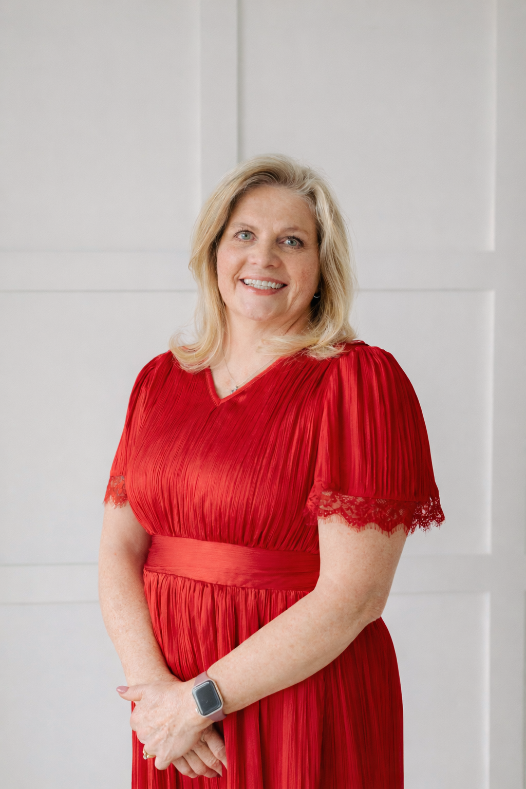 Woman in a red dress standing and smiling against a light gray wall