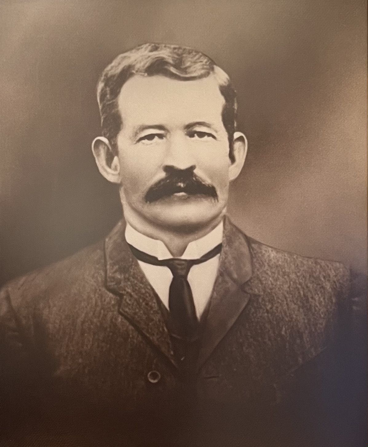 Sepia-toned studio portrait of a man in a suit and tie, facing forward with a serious expression