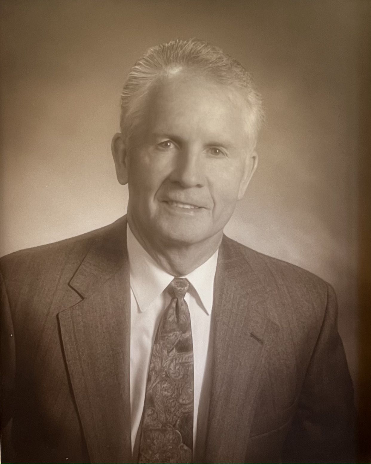 Studio portrait of a smiling man in a suit and tie against a plain background