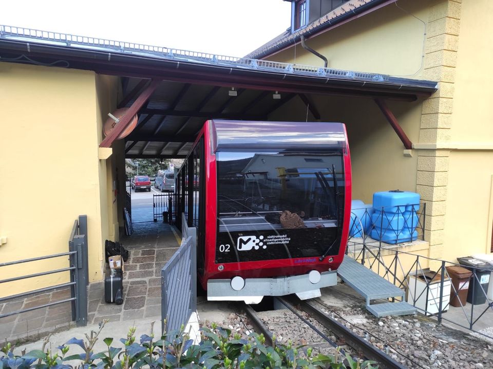 Un treno rosso è sui binari davanti a un edificio giallo