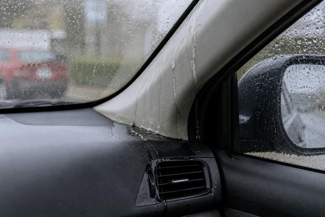 Rain-speckled car interior with side window, dashboard, and side mirror visible