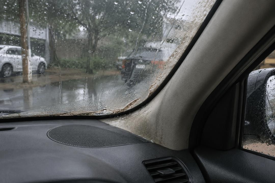 Rainy street view from inside a car, with raindrops on the windshield and parked vehicles outside.