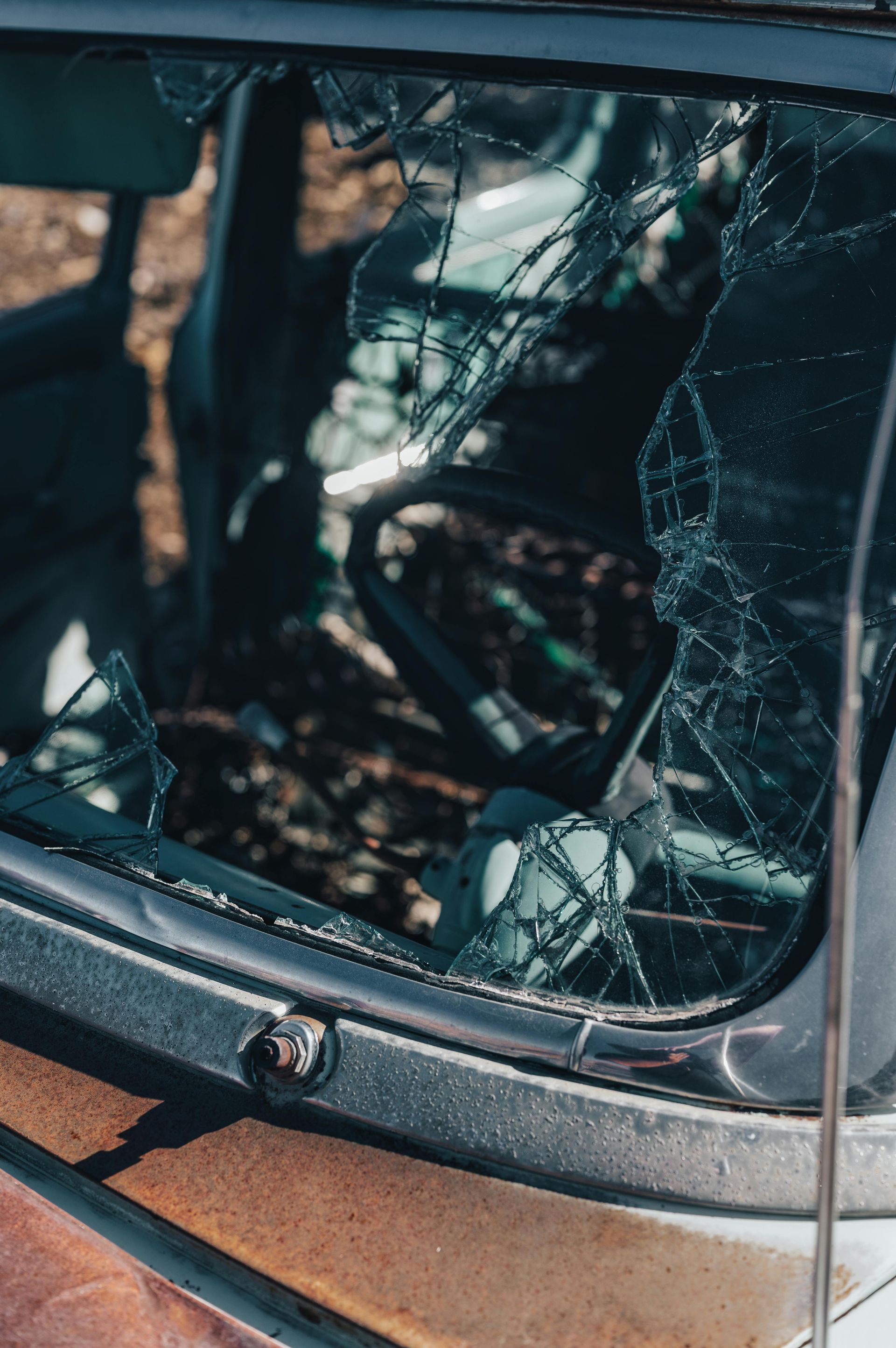 Cracked windshield of an old car, rust visible, steering wheel in view.