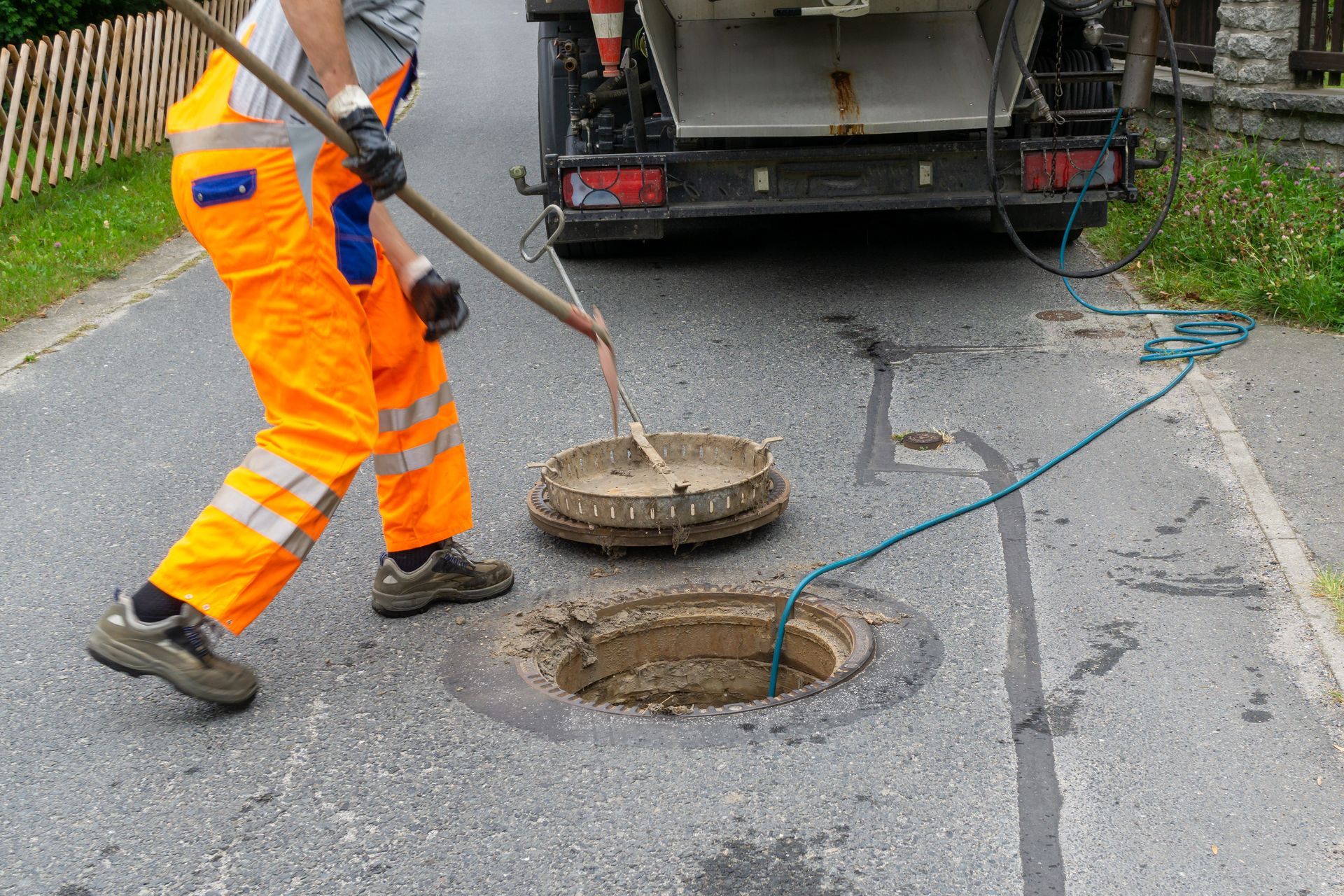 Worker in orange safety gear lifting a manhole cover on a road with an open sewer hole Worker in orange safety gear lifting a manhole cover on a road with an open sewer hole