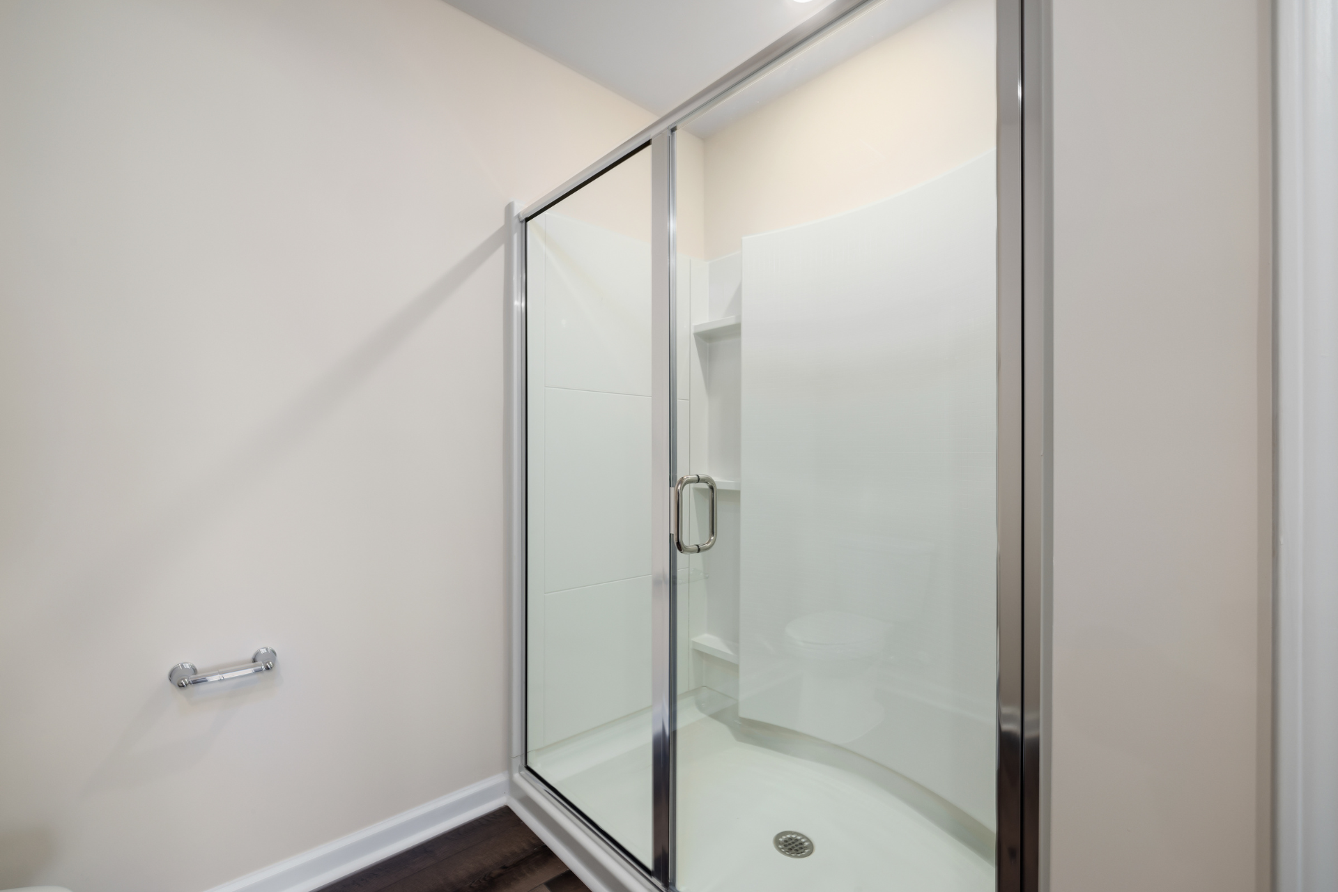 Glass shower enclosure in a bathroom with beige walls and dark flooring.