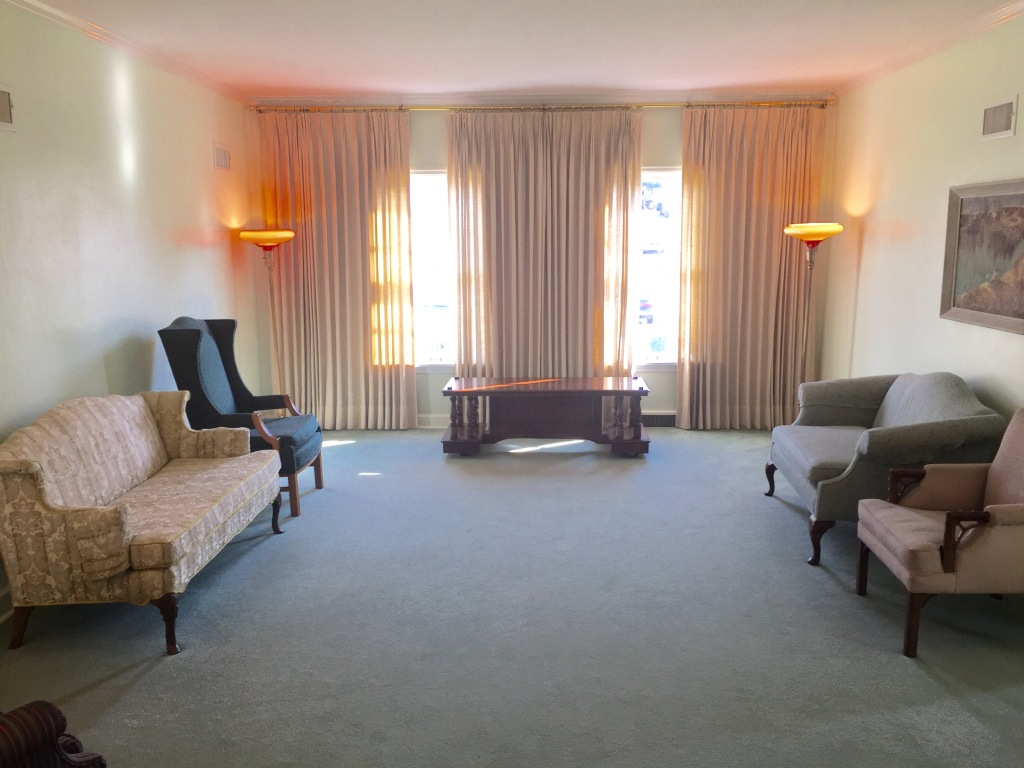 Quiet living room with beige sofas, armchairs, curtains, and warm wall lamps facing a coffee table.