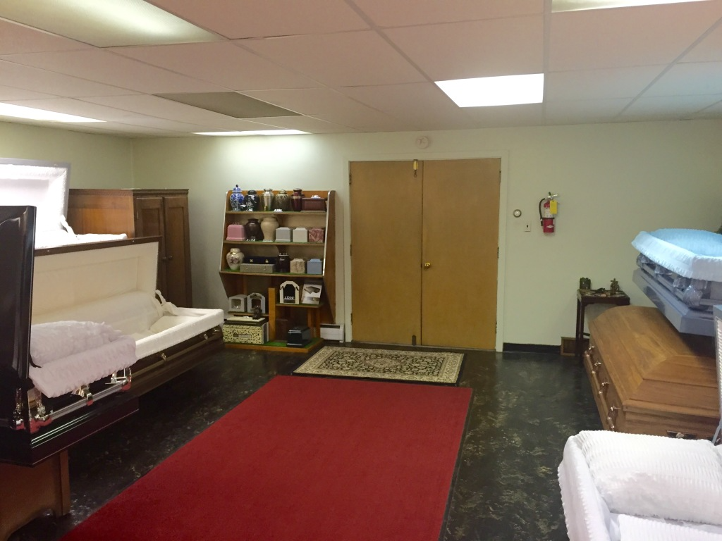 Empty room with cots, a red rug, shelving, and double doors under fluorescent lights