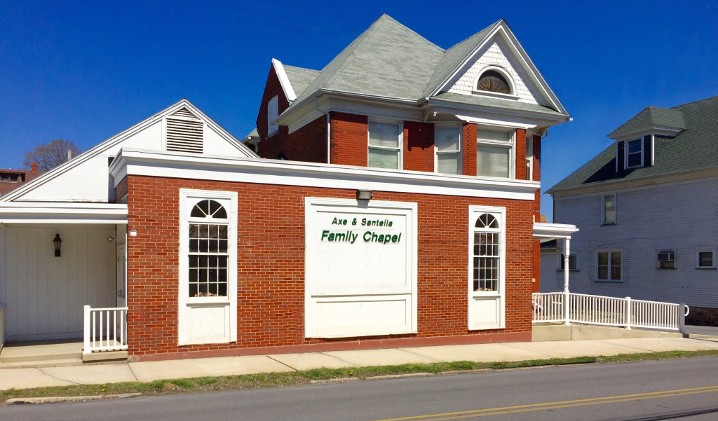 Red brick storefront with white trim and a central sign, on a sunny street under a blue sky