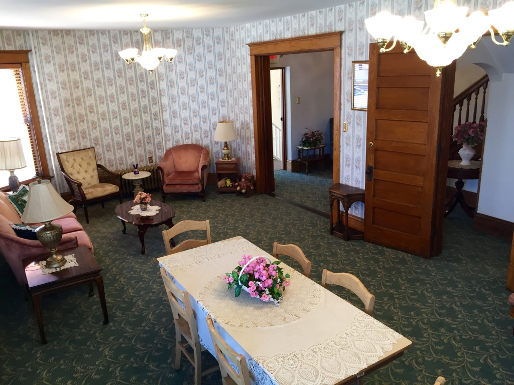 Living room with floral wallpaper, green carpet, furniture, and a dining table with flowers