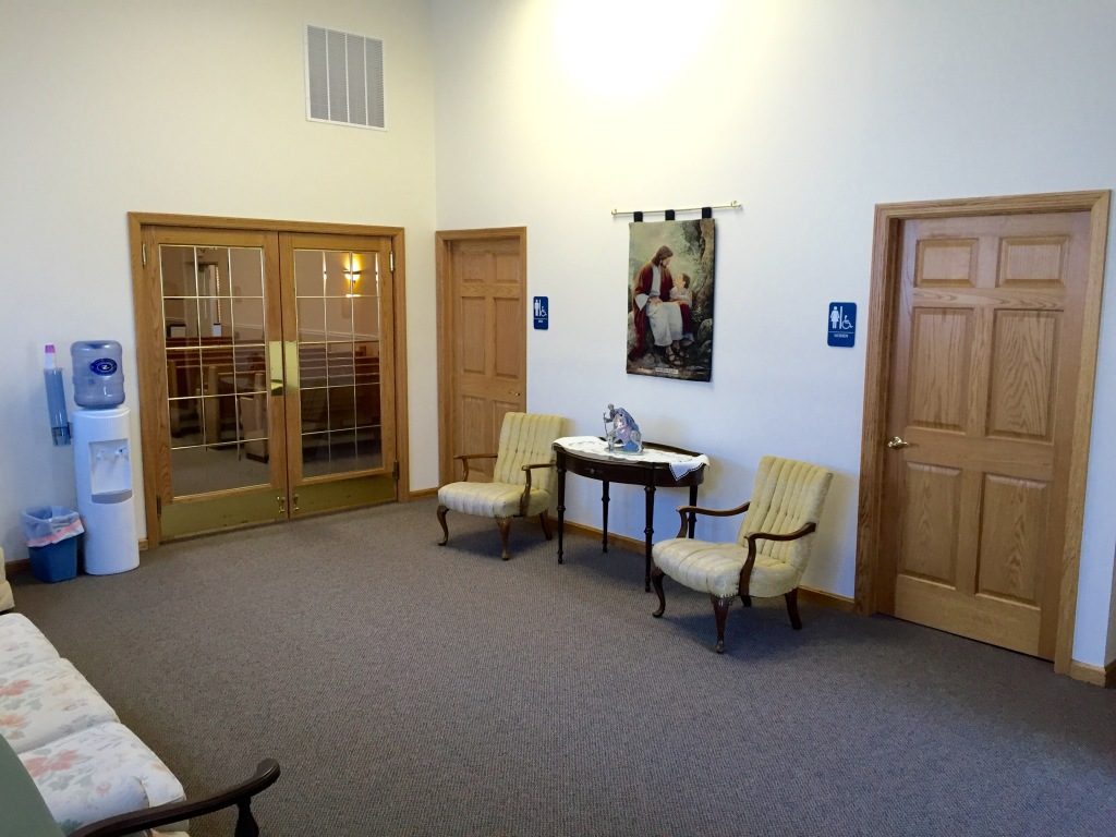 Quiet office waiting room with chairs, a small table, framed art, and wooden doors on white walls.