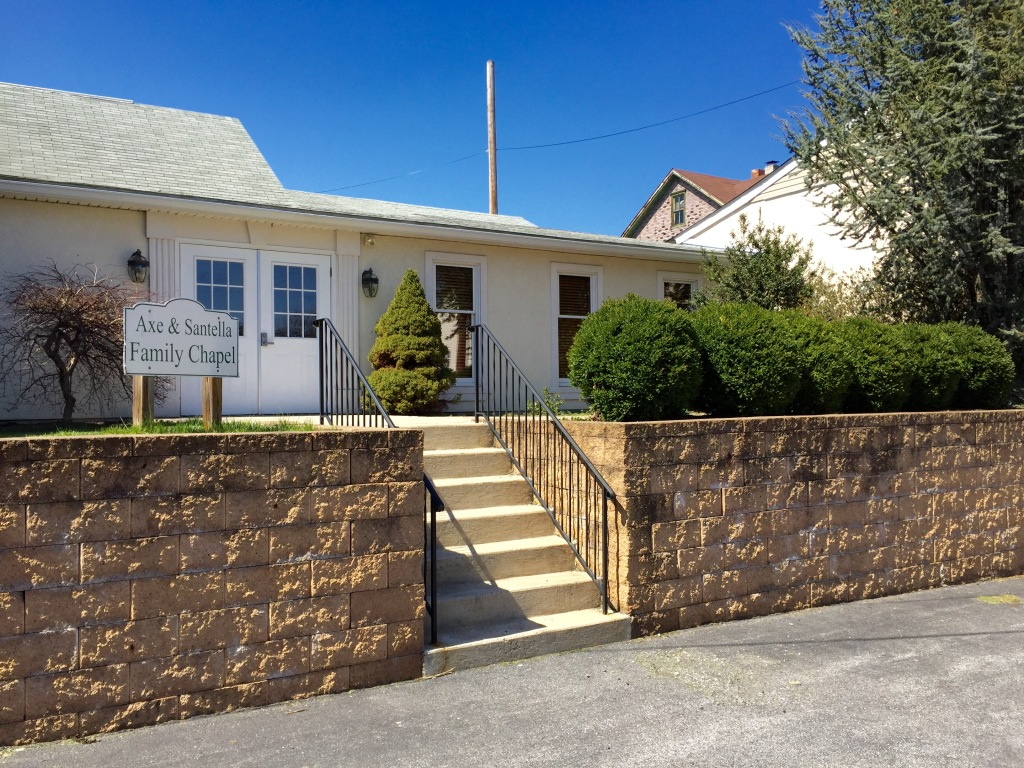 Single-story white house with steps, brown stone walls, and trimmed shrubs under a blue sky