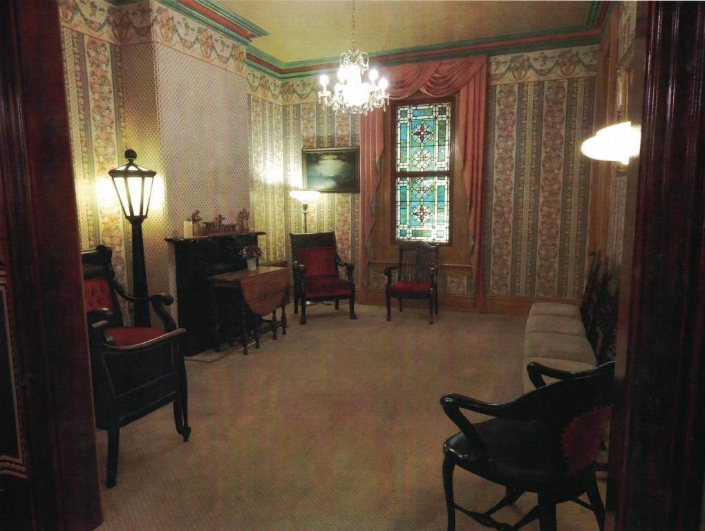 Vintage room with patterned wallpaper, stained-glass window, chairs, lamp, and a chandelier