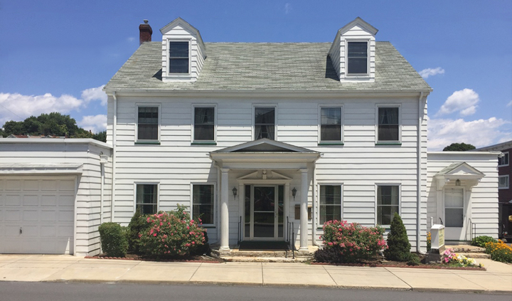 White two-story house with dormer windows, a front porch, and a garage under a partly cloudy sky