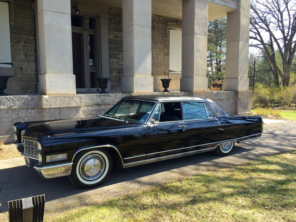Black classic car parked by a stone building with columns.