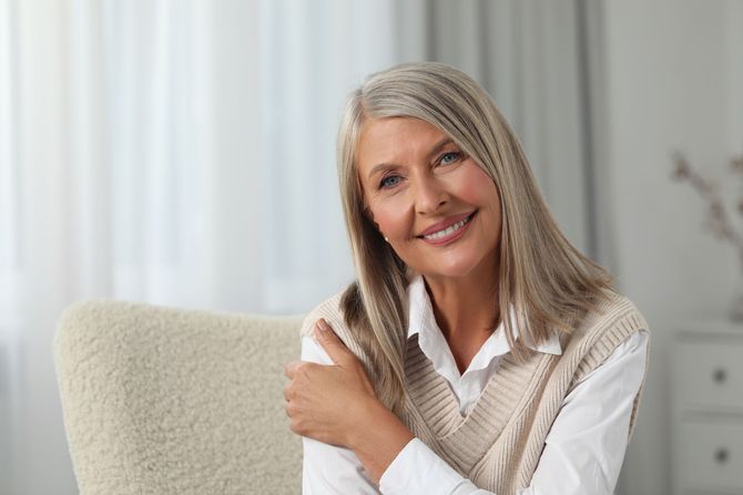 A woman in a white towel is smiling and touching her neck