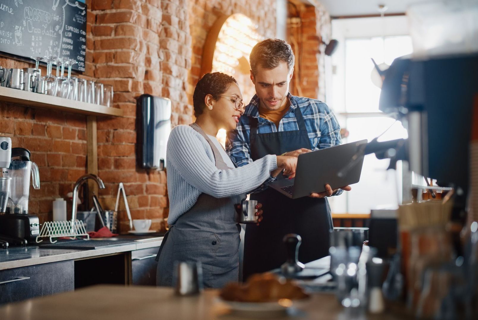 A man and a woman are looking at a laptop in a restaurant.
